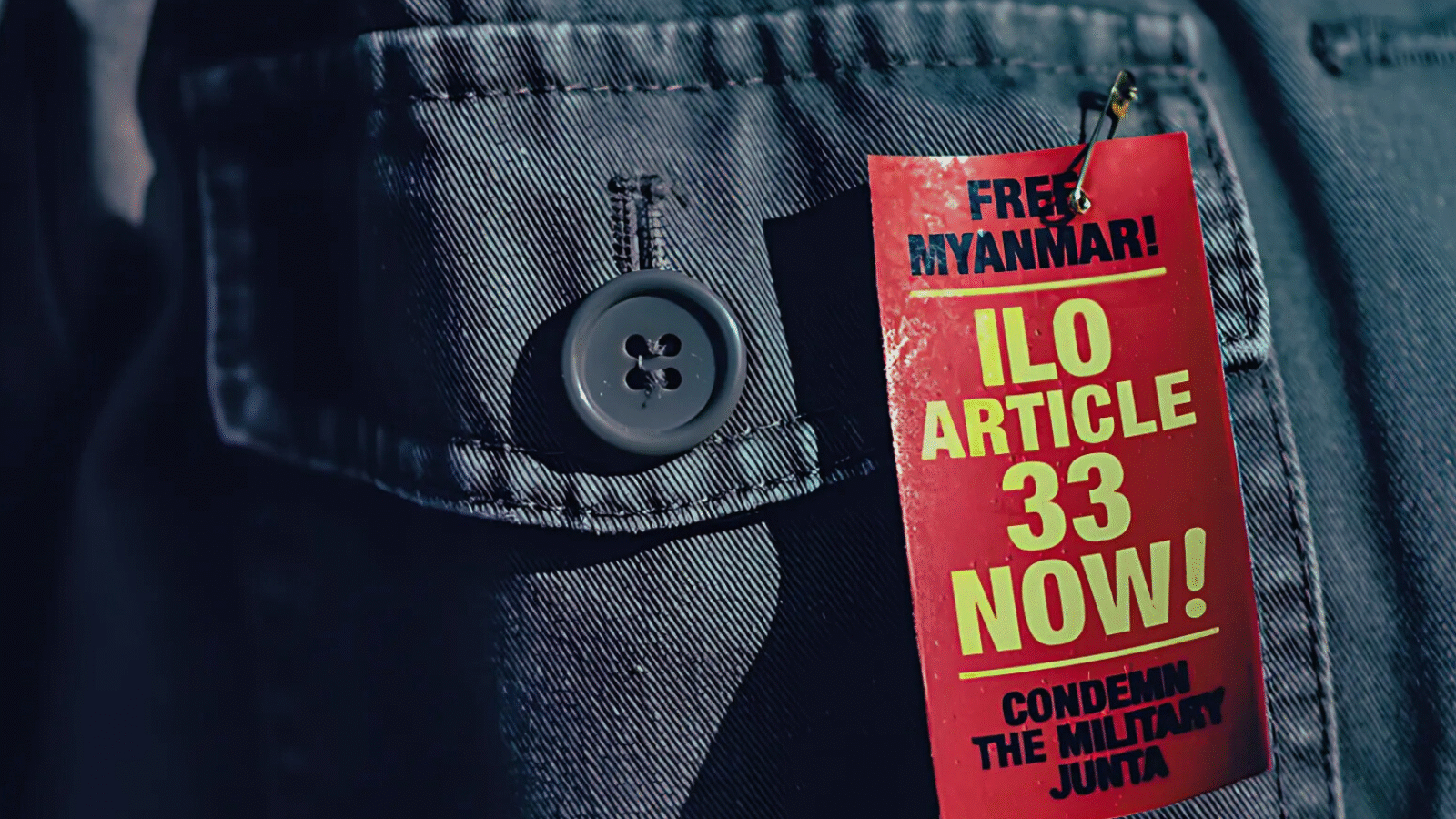 Red campaign tag on a jacket reading "Free Myanmar, ILO Article 33 Now, Condemn the Military Junta" at a demonstration in Geneva, 2024.