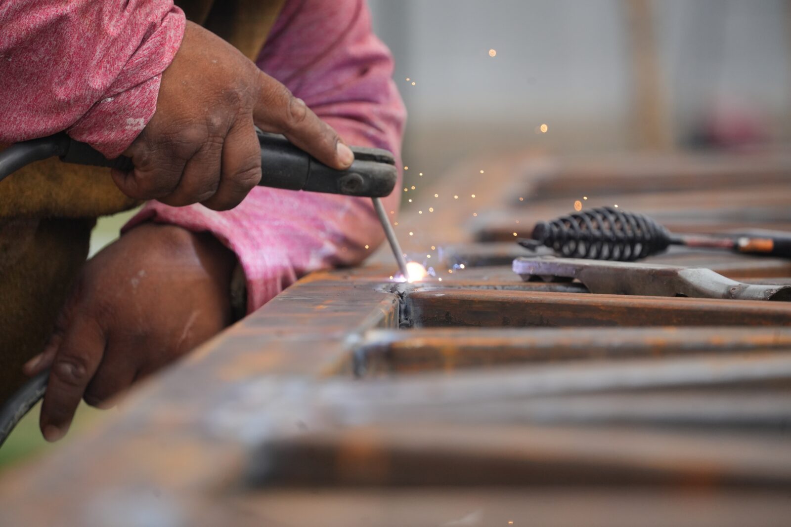 Migrant worker welding metal trusses, close-up of hands and sparks